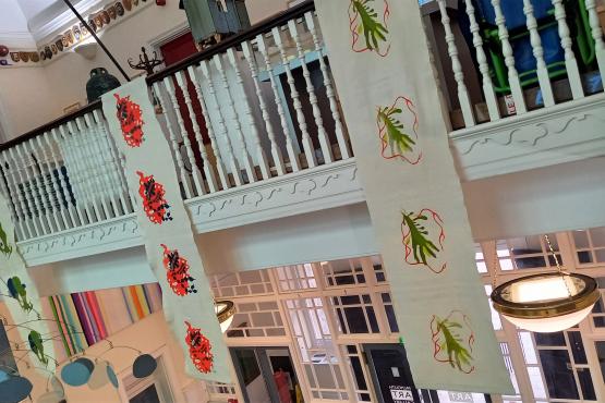 Banners hanging from a balcony in a big public space. The banners have colourful prints on them inspired by seaweed.