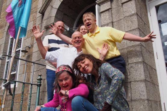 A group of 6 people standing on steps. Some people are crouched and some are standing behind them. They are all looking at the camera and smiling.