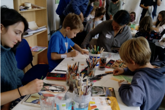 A group of people and children drawing in sketchbooks on a table full of art materials