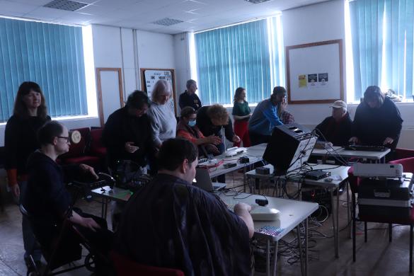 A group of people playing with electronic instruments around tables