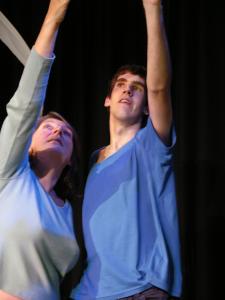 2 people performing. They are standing close together, each with one arm raised above their head. 