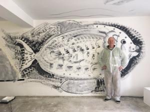 A person standing in front of large black and white drawing on the wall of a fish