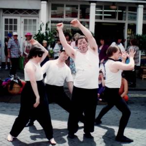 4 people dancing in white vests and black trousers on the street for Mazey Day parade.