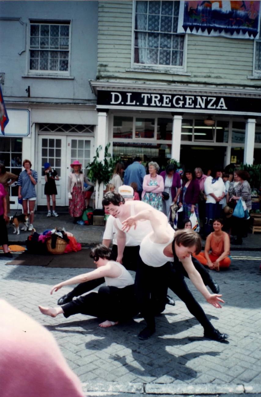A group of people performing in the street at Mazey Day. They are dancing and their is a crowd around them watching. 