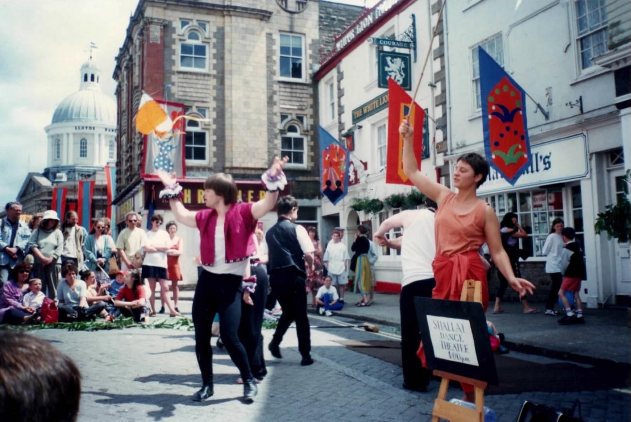 A group of people performing in the street at Mazey Day. They are dancing and their is a crowd around them watching. 