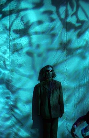 A man in sunglasses performs against a backdrop of projected blue light