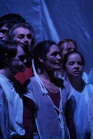 6 performers in the Mask performance wearing white standing on a blue stage