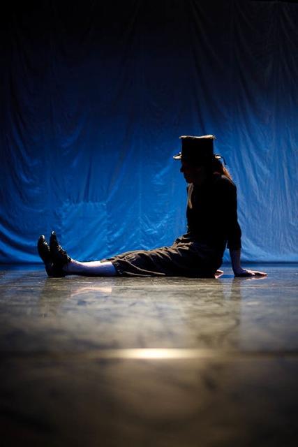 A person performing on stage. The person is visible in silhouette against a blue background.  